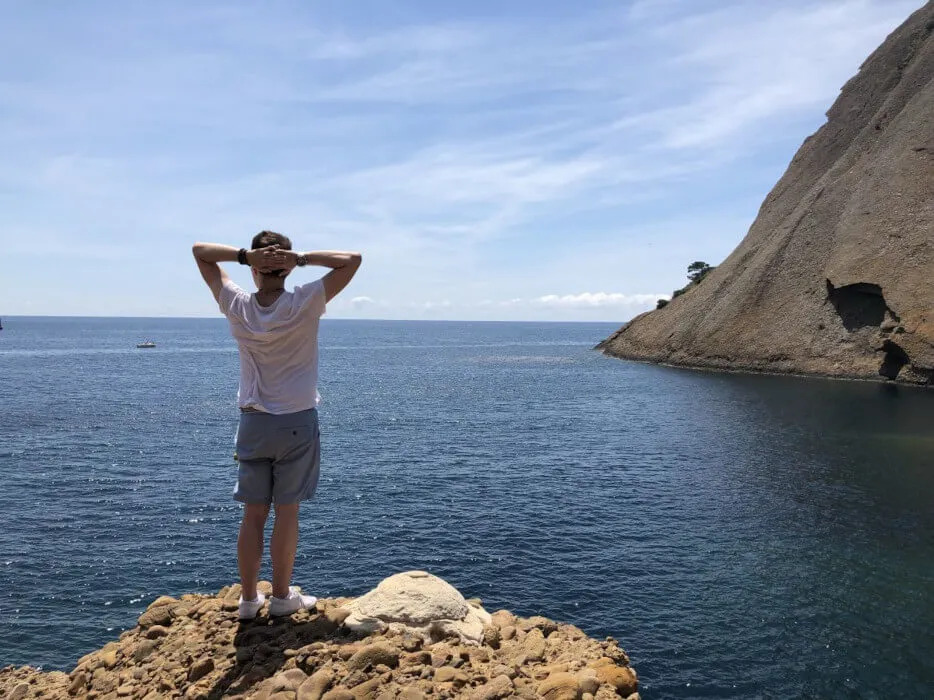 A person in casual wear looking out to sea comfortably. To their right, a cliff meets the ocean.